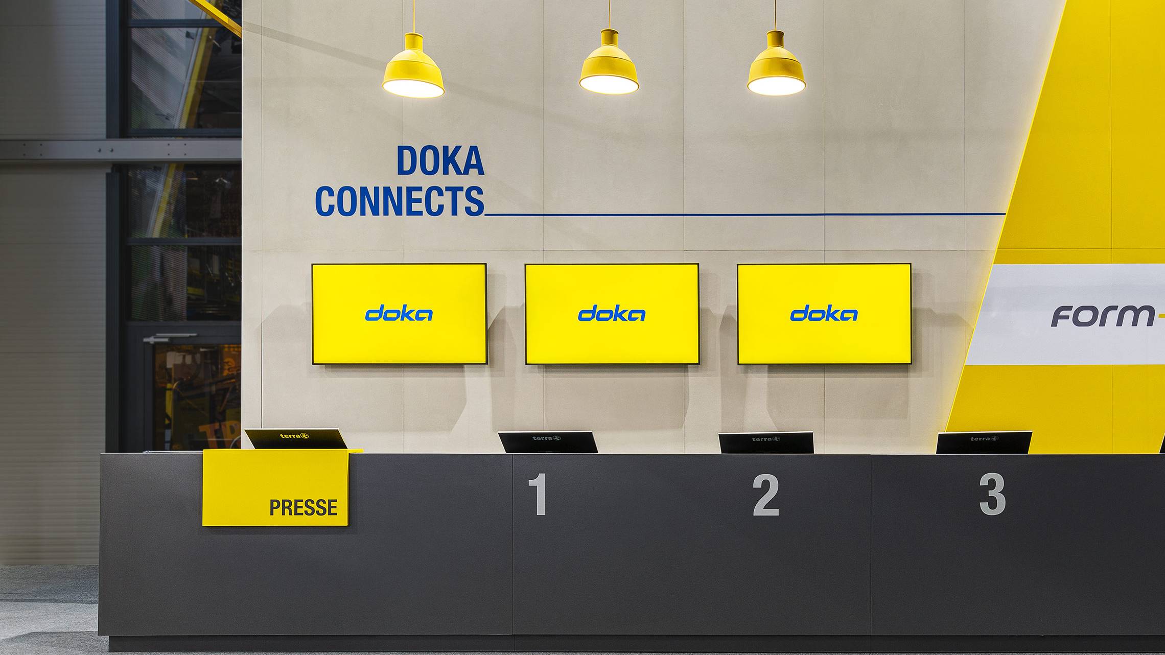 Frontalaufnahme einer Empfangstheke im Messezelt von DOKA bei der bauma 2022 in München, gestaltet in Gelb und Blau mit industriellen Designelementen.