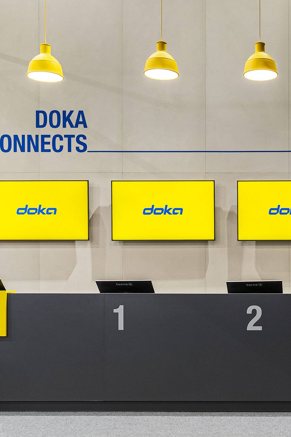 Frontalaufnahme einer Empfangstheke im Messezelt von DOKA bei der bauma 2022 in München, gestaltet in Gelb und Blau mit industriellen Designelementen.
